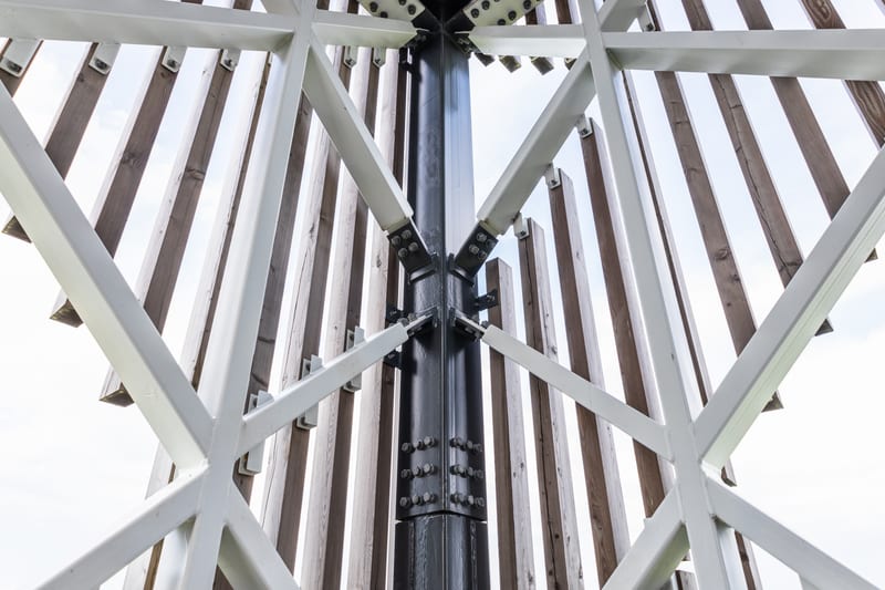 A dark steel column with white bracing members bolted to it, seen from below.