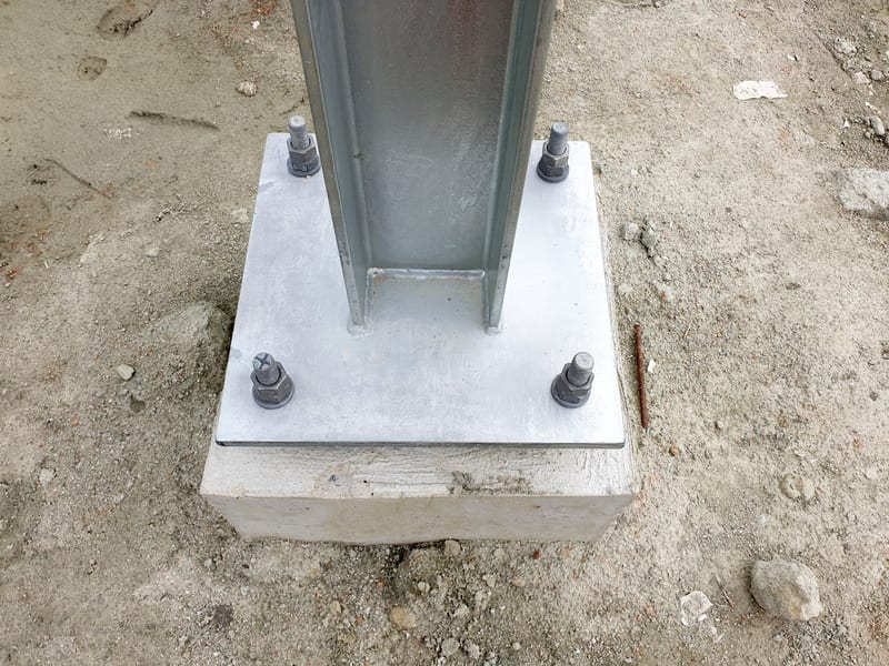 A galvanised steel column base plate bolted down to a concrete pedestal on site.