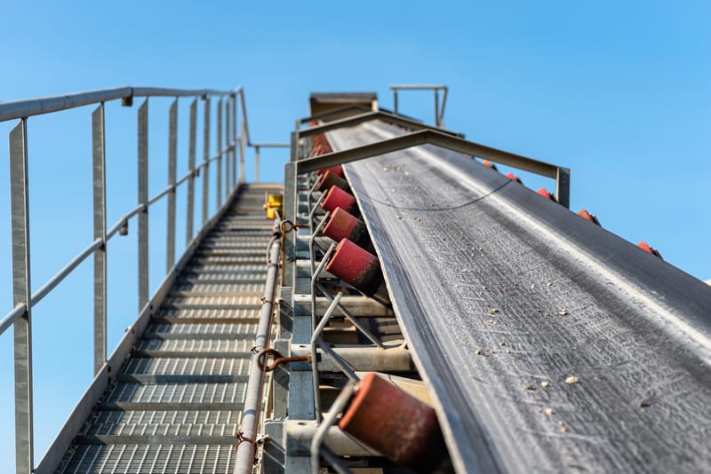 An inclined conveyor belt on a steel gantry with transport rollers.