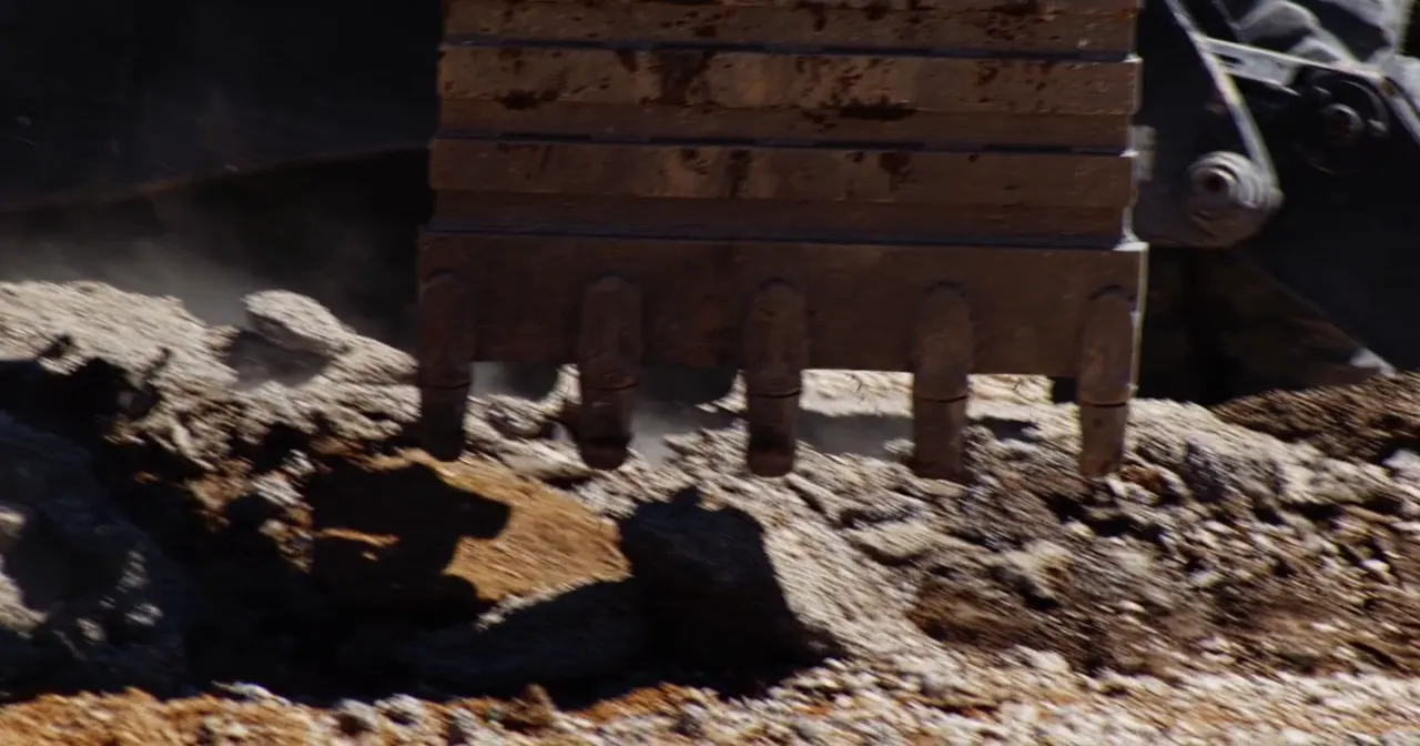 An excavator bucket breaking out ground.