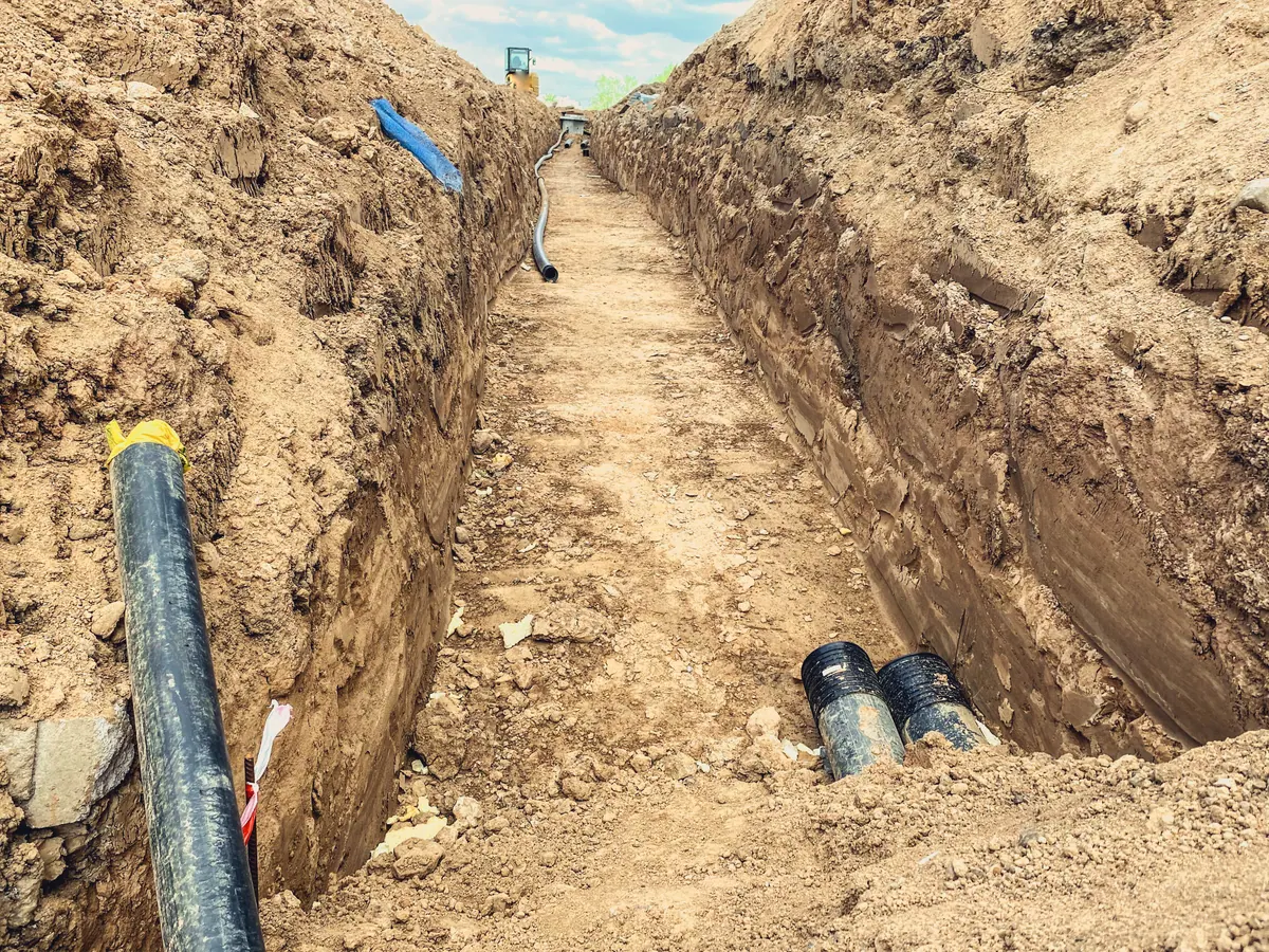 An open trench cut through clay, with pipes laid along its floor.