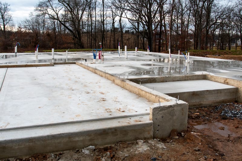 Cured concrete footings and slab edge on a cleared site, with steel set into the pour.